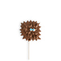 A chocolate monster lollipop with a brown textured body, small blue and white eyes, and a thin white stick, centred on a plain white background.