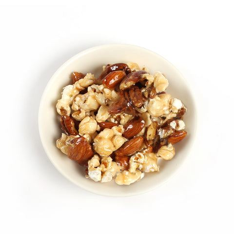 A mix of buttery rich, caramel coated pecans, almonds and fresh popcorn, packaged in a paper bag with a clear window.