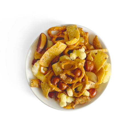 A bowl full of a new twist on a classic snack mix! Contains corn chips and corn puffs, hickory sticks, everything sesame sticks, honey sticks, mini pretzels, salted peanuts, brazils and cashews.